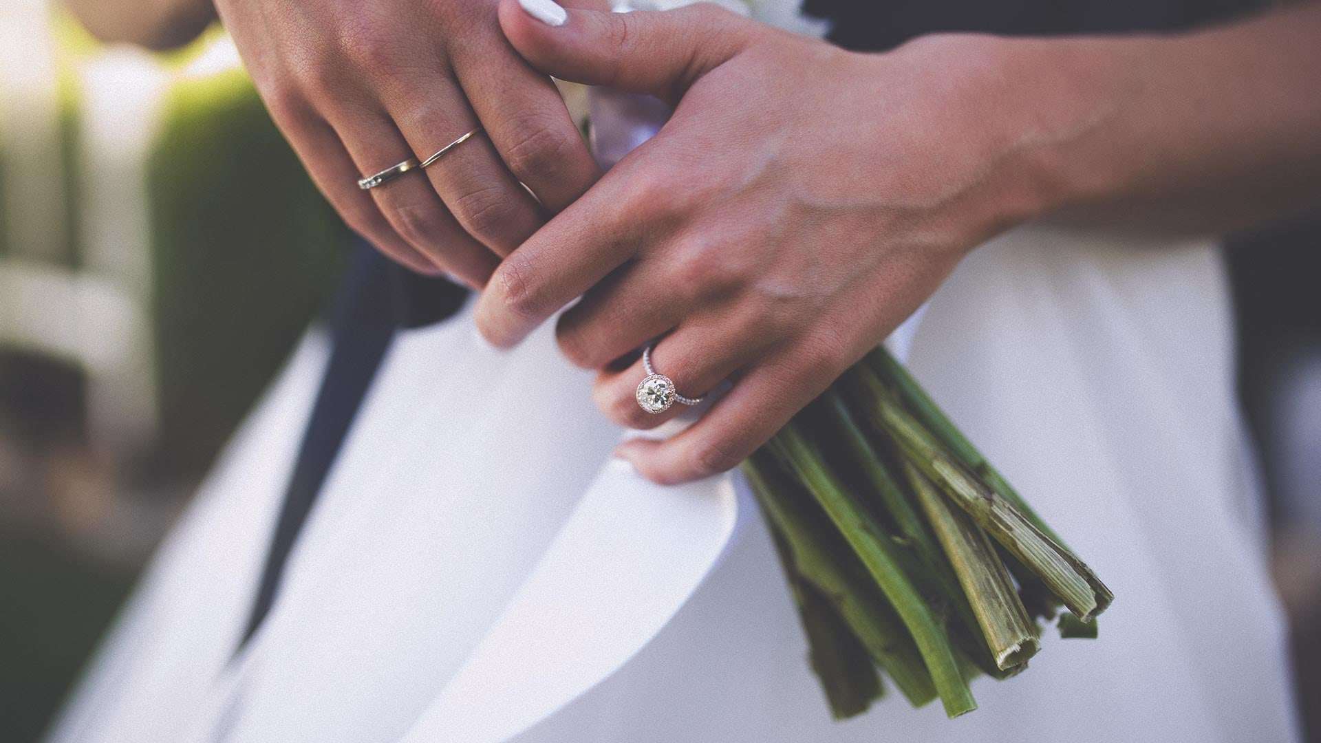 Mains de la mariée sur son bouquet, bague de fiançailles et alliances