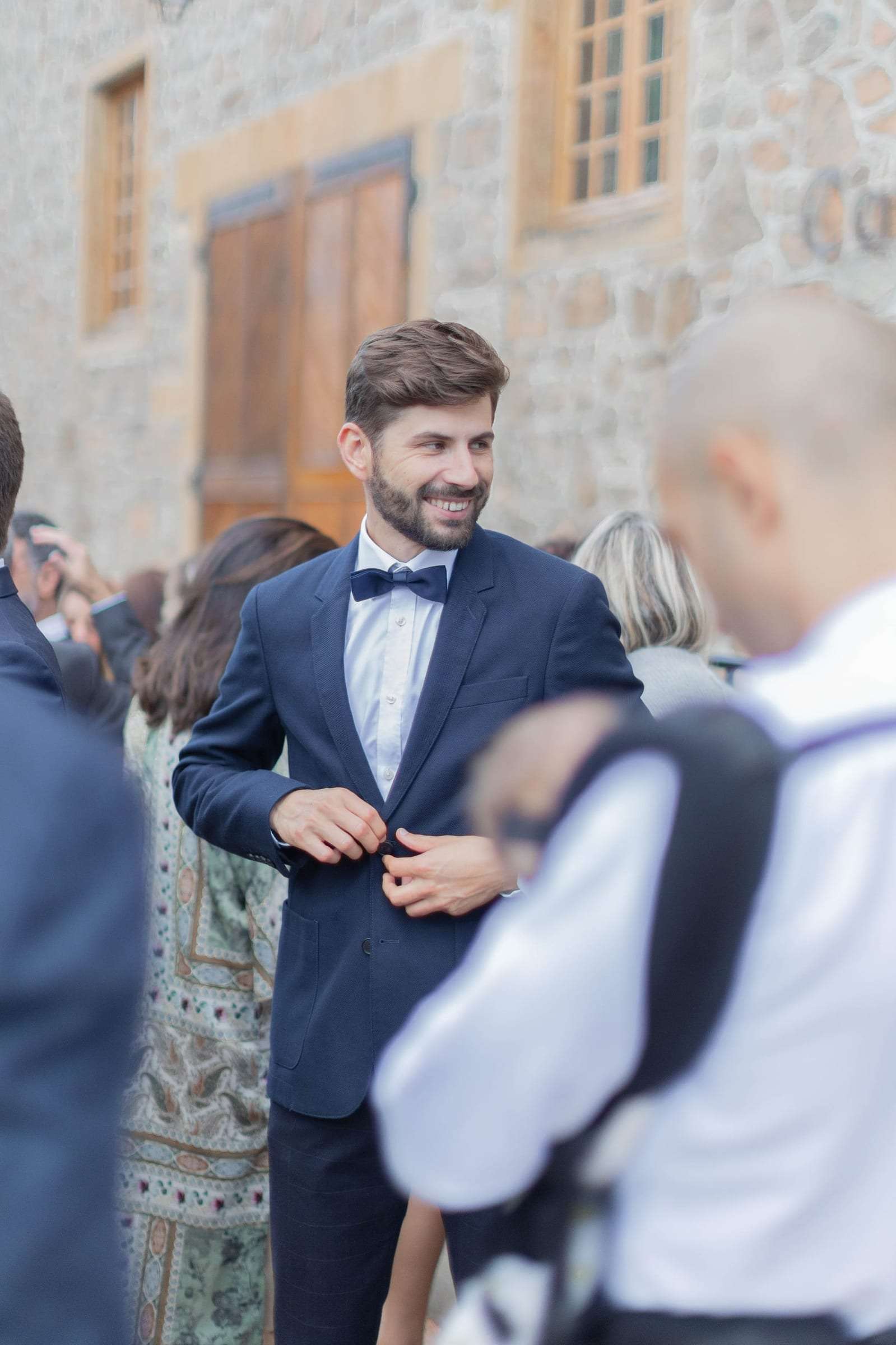 Le marié en costume bleu rit avec un invité dans la cour en pierre
