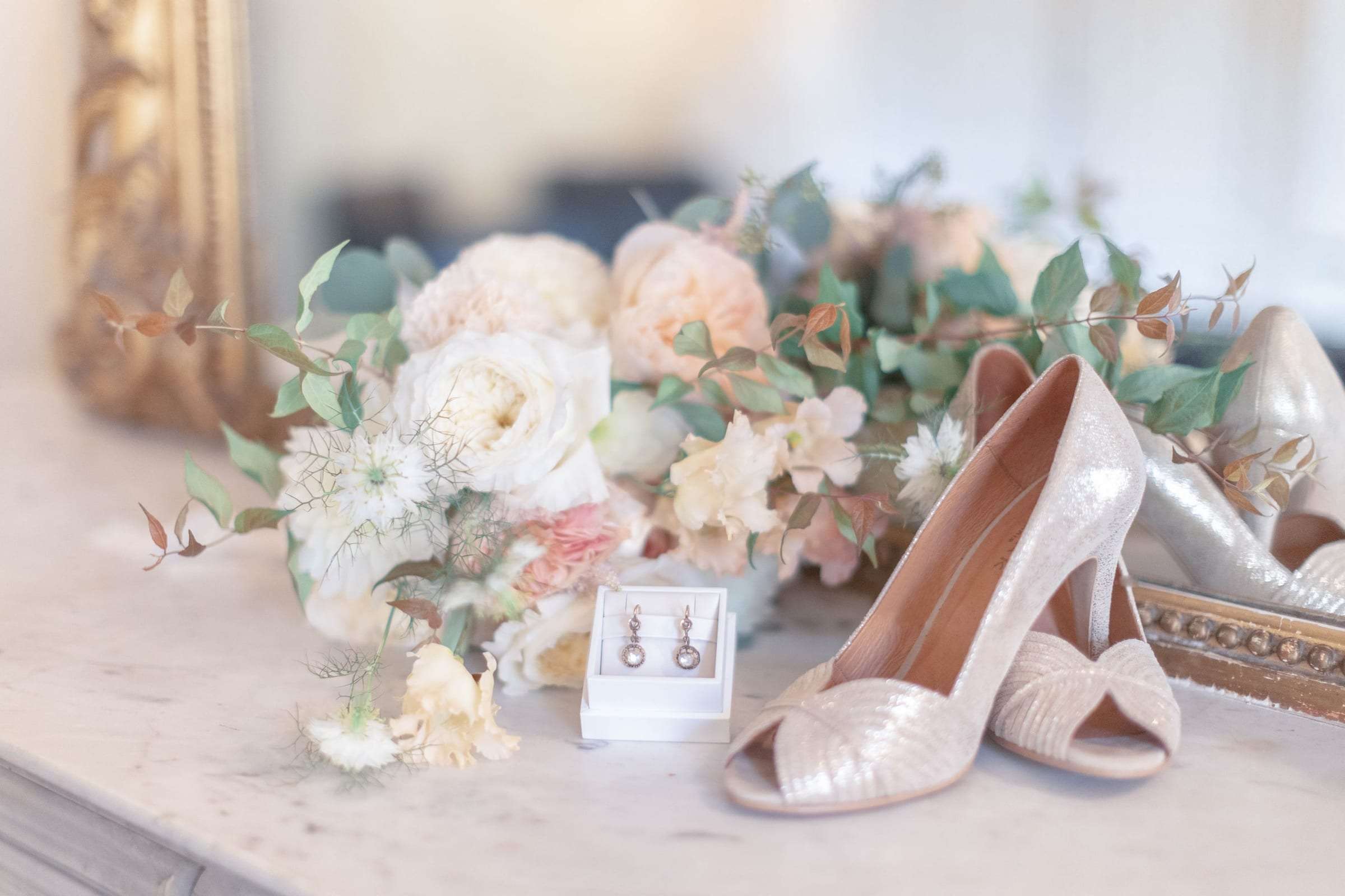 Escarpins nacrés et fleurs pastel posés sur une commode au miroir doré