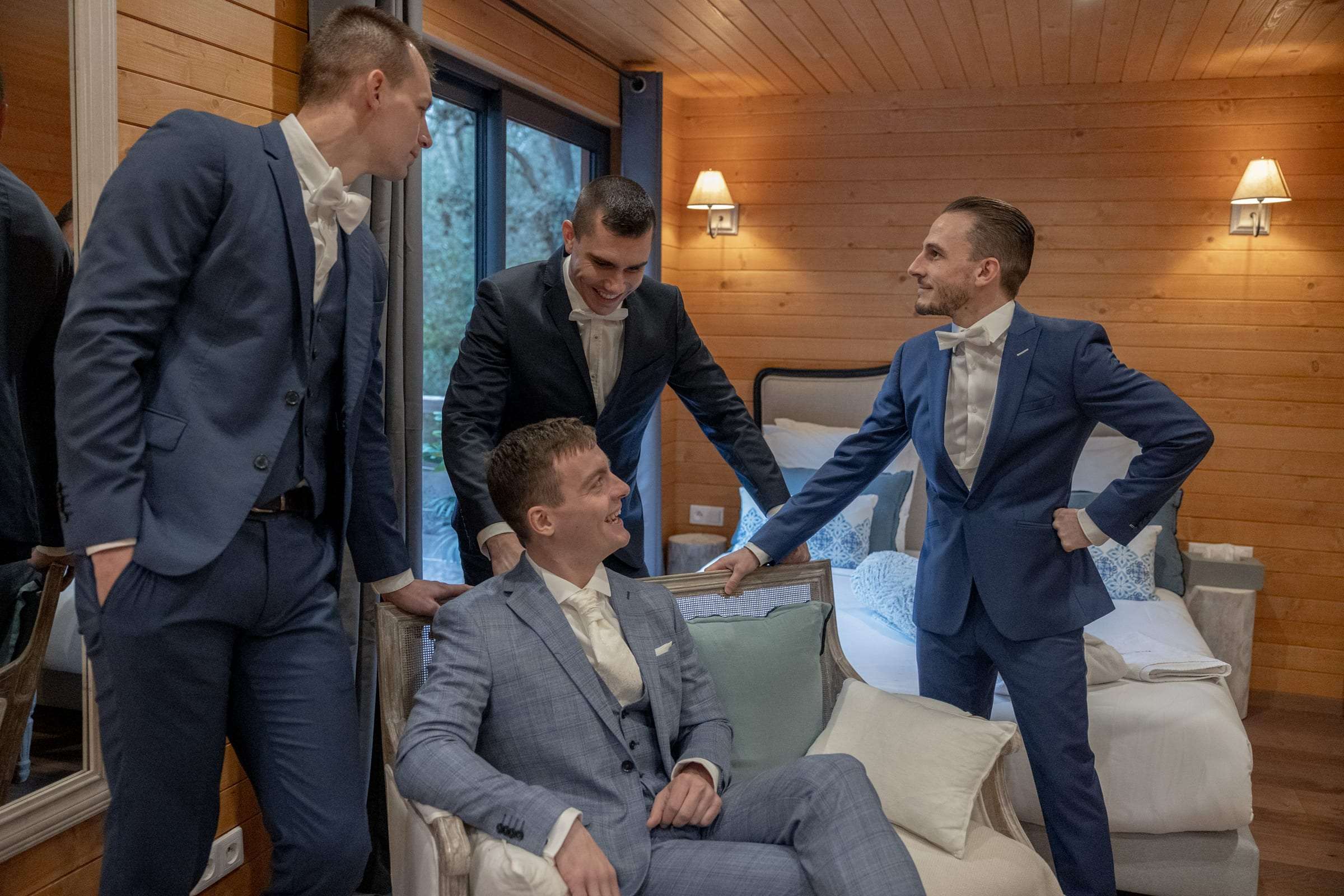 Le marié et ses témoins rient ensemble pendant les préparatifs, dans une chambre lambrissée de bois