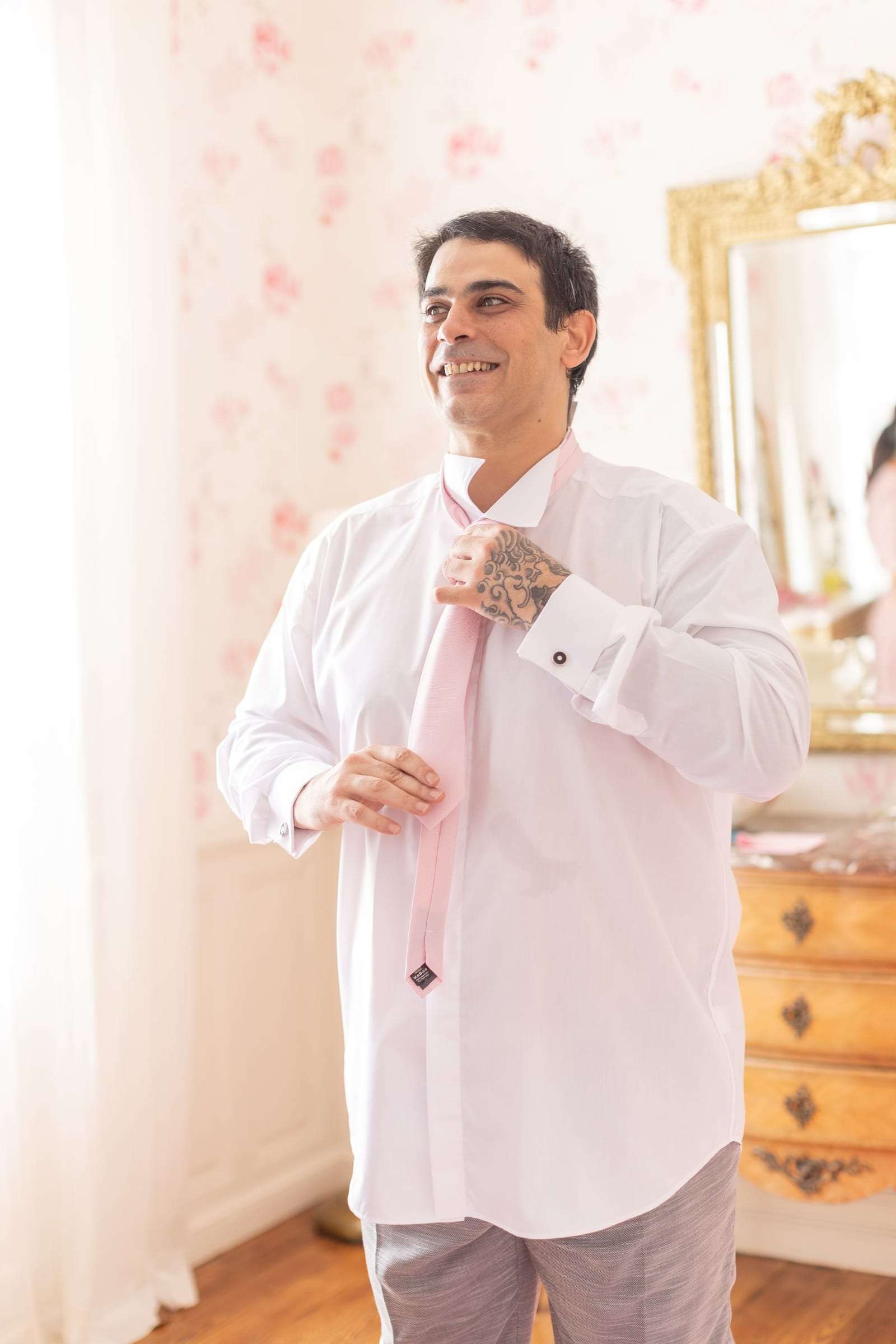 Le marié noue sa cravate rose devant un miroir doré