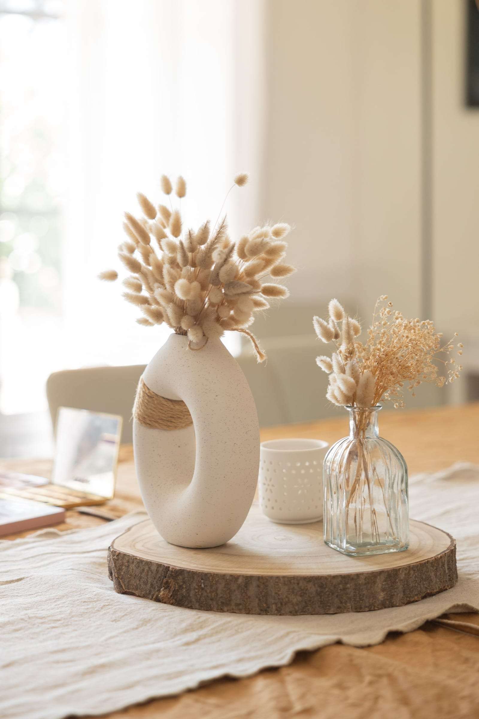 Vase blanc et fleurs séchées sur un rondin de bois, décoration de table