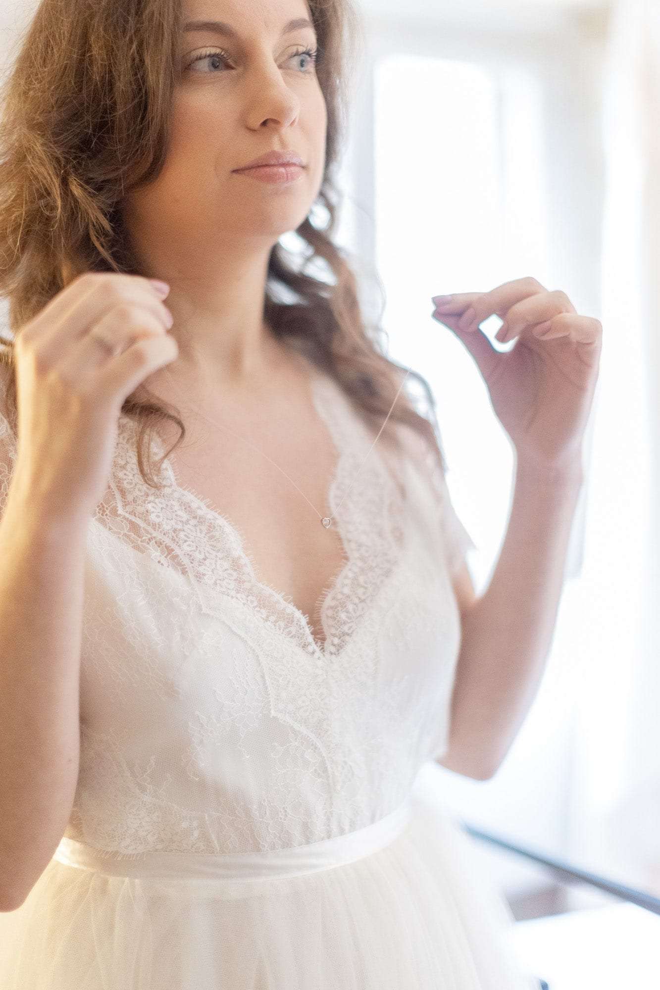 La mariée met ses boucles d'oreilles près de la fenêtre