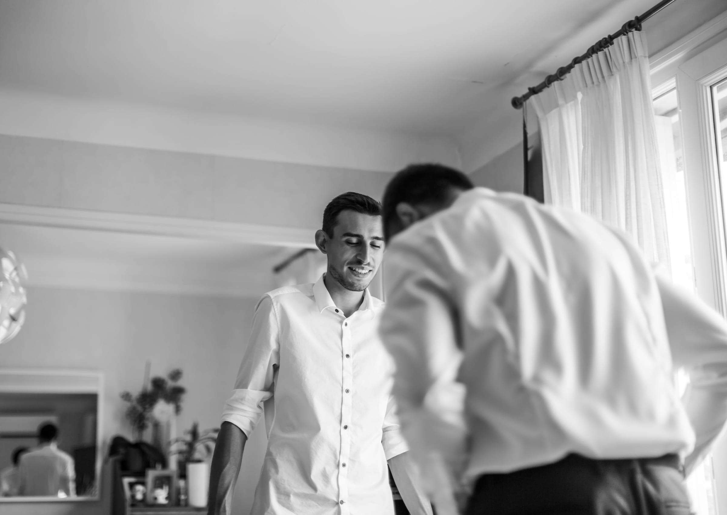 Photo noir et blanc du marié aidé à enfiler sa chemise