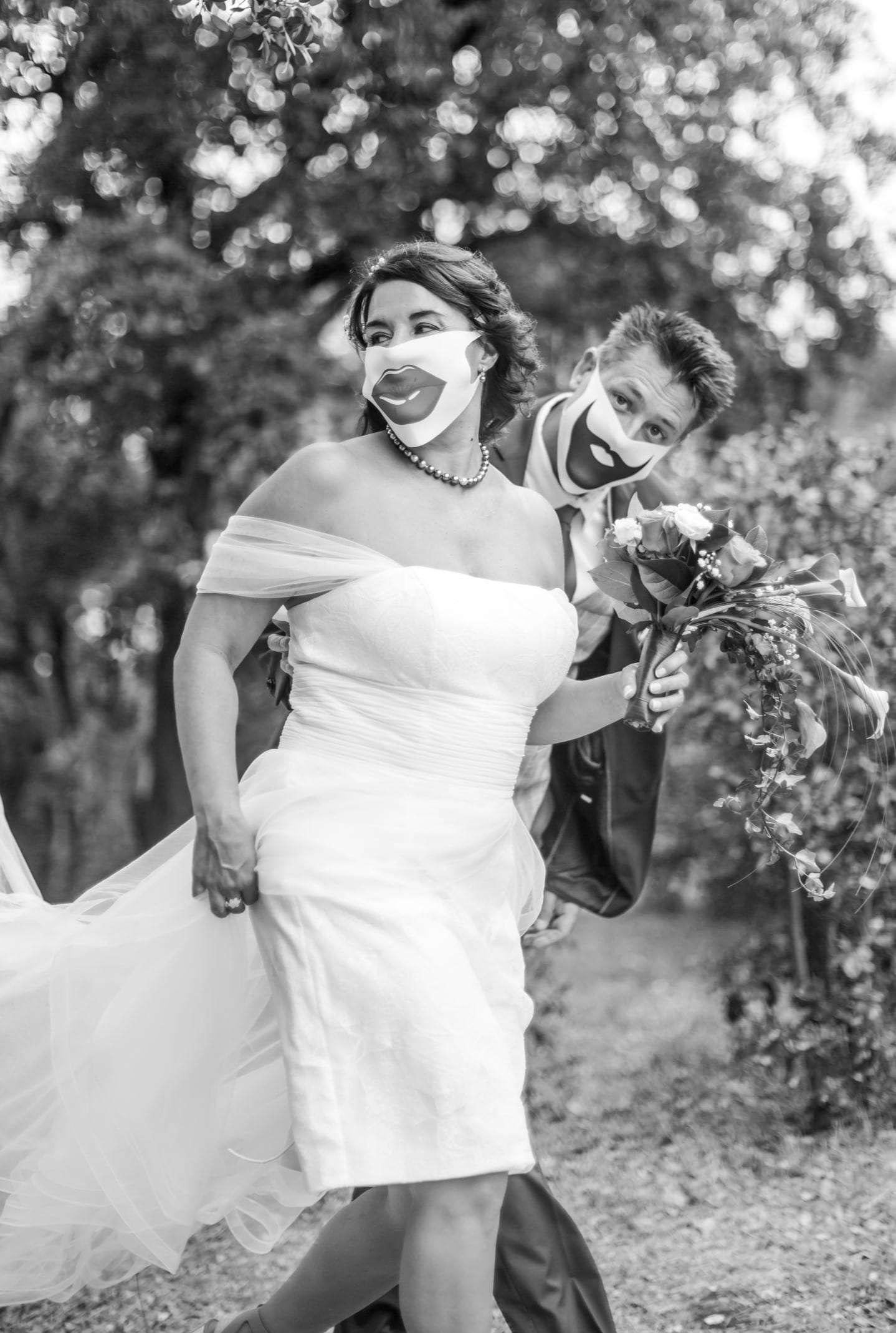 Photo noir et blanc de la mariée qui marche en riant, bouquet à la main