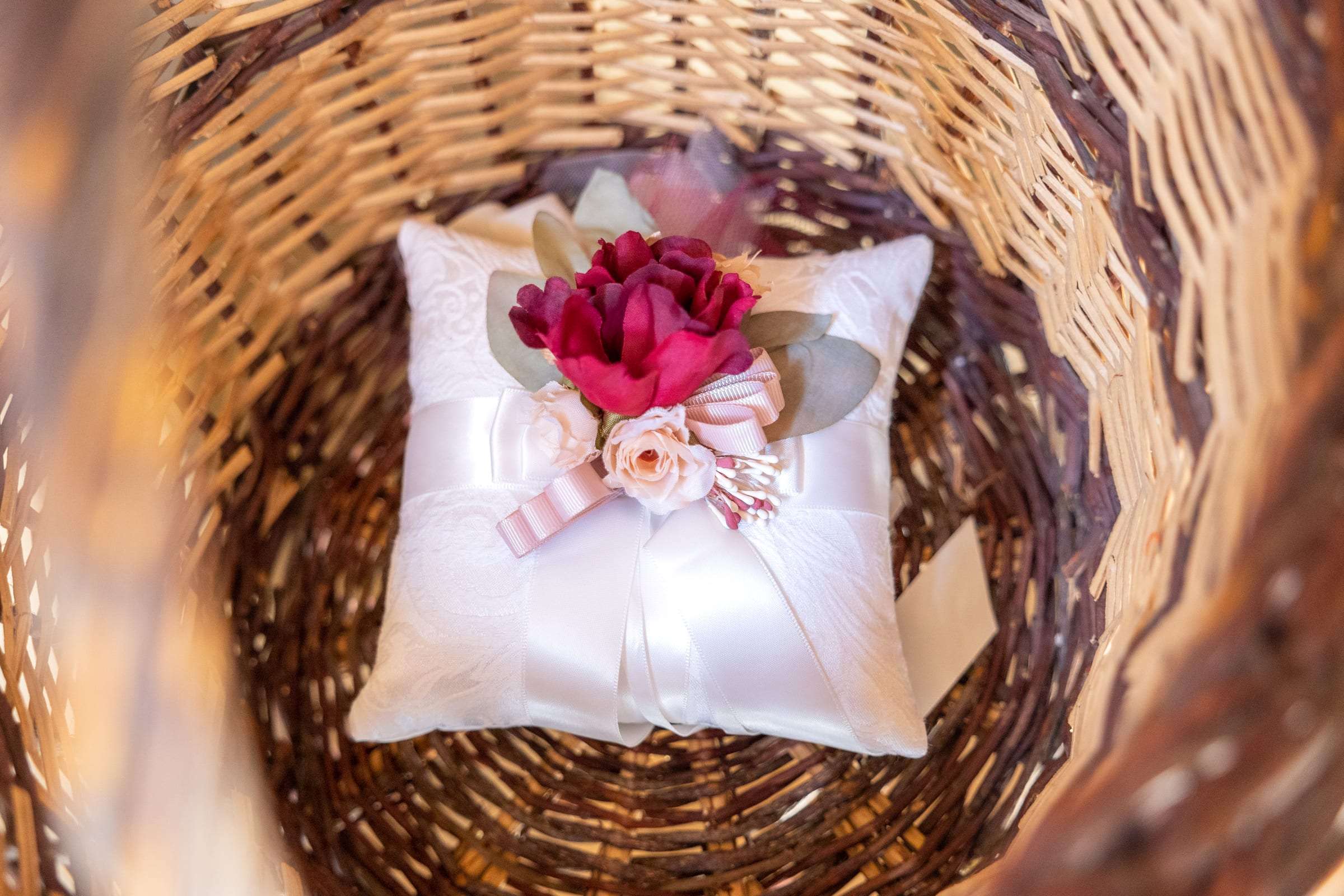 Coussin d'alliances blanc et fleurs rouges dans un panier en osier